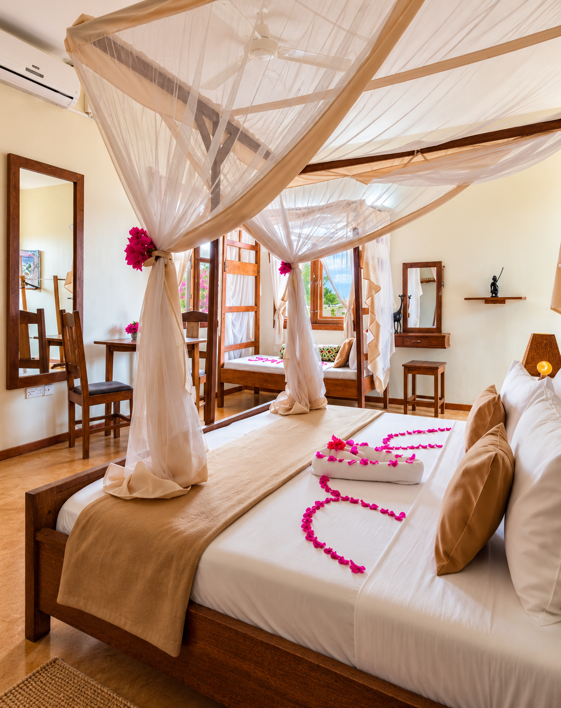 Four-poster bed with white mosquito netting and pink flowers in a guest room at Sand Bank View Hotel